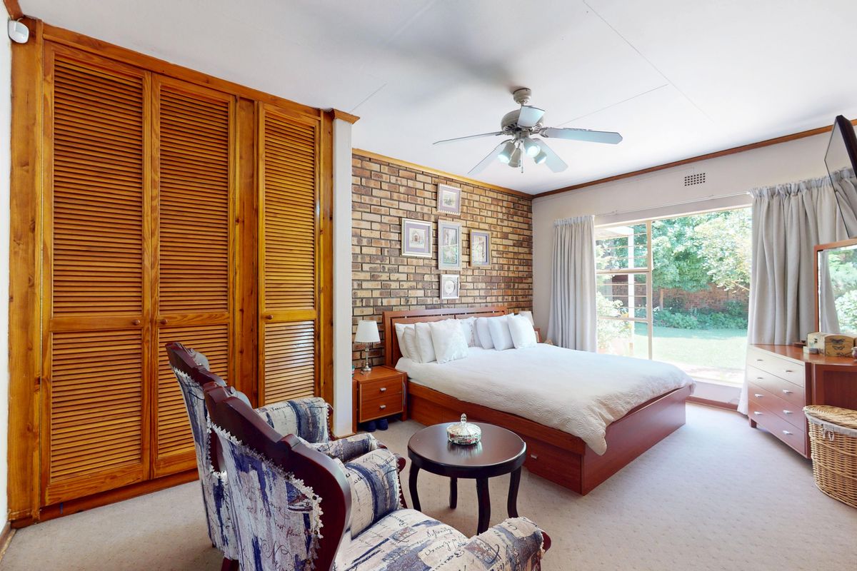 Spacious bedroom featuring an exposed brick wall, built-in wooden louvered wardrobes, a ceiling fan, and direct access to the garden through a sliding glass door.