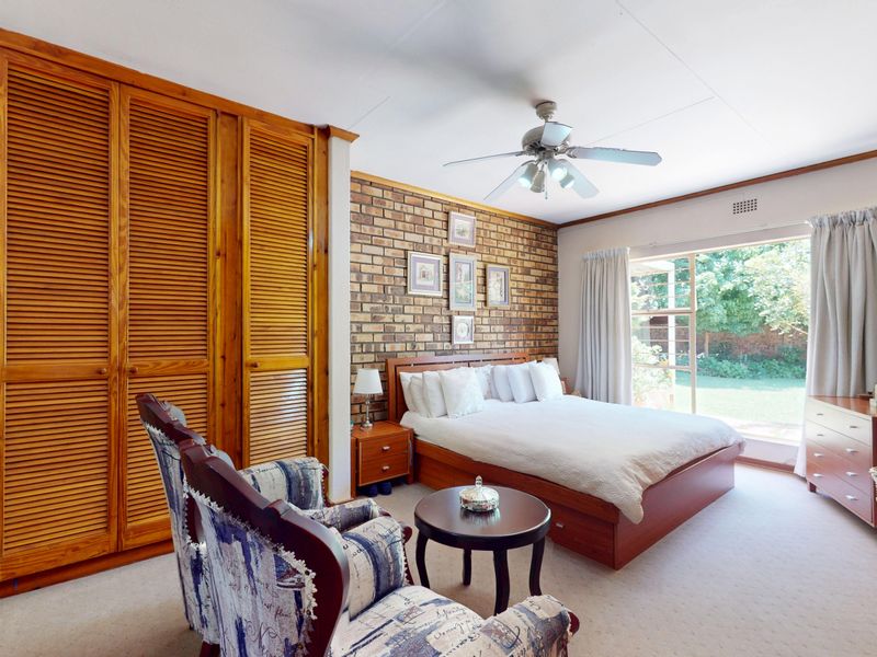 Spacious bedroom featuring an exposed brick wall, built-in wooden louvered wardrobes, a ceiling fan, and direct access to the garden through a sliding glass door.