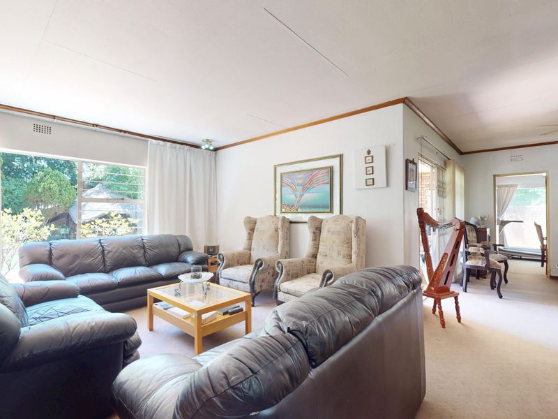 Spacious living room featuring large windows, neutral carpeting, and a ceiling fan, offering a comfortable and well-lit area for relaxation.