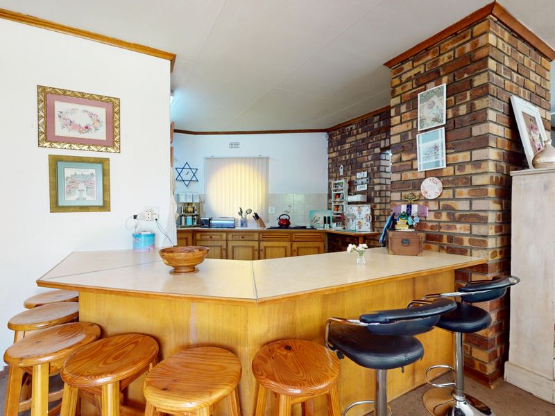 Open plan kitchen and living area featuring a prominent brick pillar, wooden cabinetry, and a built-in breakfast bar counter.