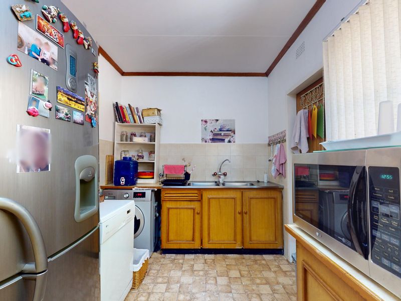 A functional kitchen area featuring wooden cabinetry, a double sink, and tiled backsplash, offering potential for modernization and aesthetic updates.