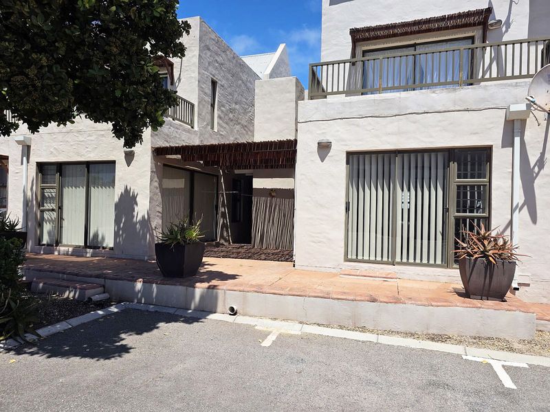 Front elevation of an apartment complex featuring a terracotta tiled patio, sliding glass doors with vertical blinds, and a covered pergola entrance.