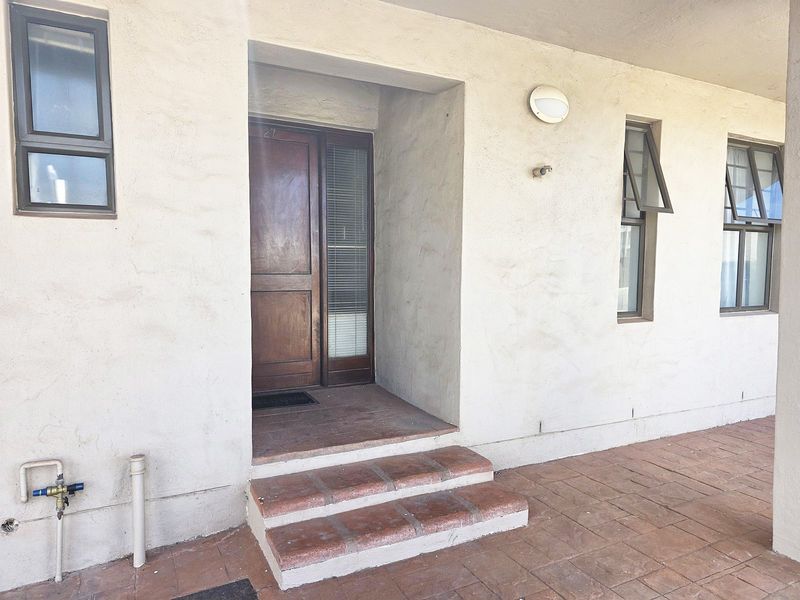 Entrance area featuring a timber front door, terracotta tiled steps, and exterior wall lighting, showing signs of weathered plaster and paintwork.