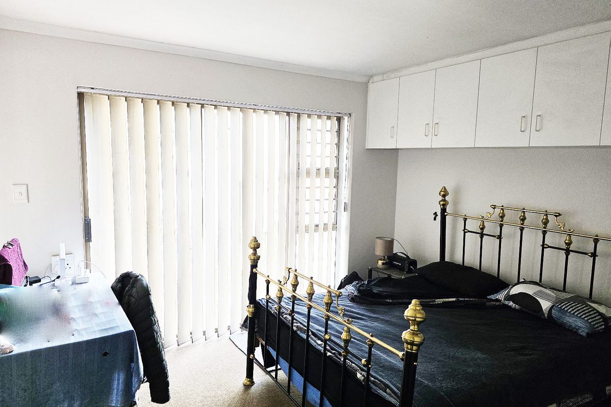 A bedroom featuring built-in overhead cupboards, carpeted flooring, and a sliding door with vertical blinds providing natural light.