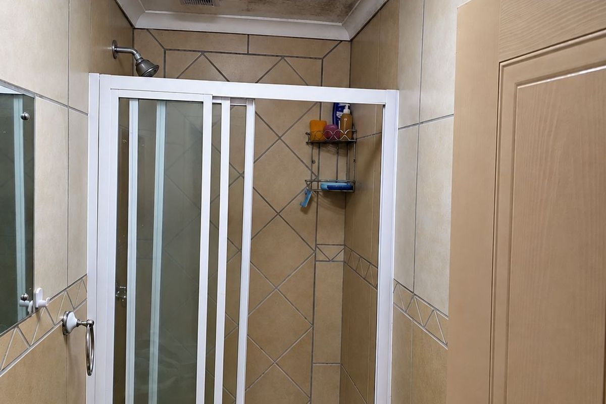 A compact bathroom featuring a shower enclosure with tiled walls and flooring, requiring attention to ceiling maintenance.