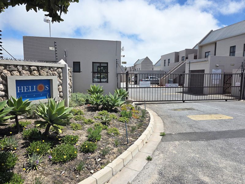 Front entrance view of Helios Place apartment complex featuring a secure gated access point, electric fencing, and well-maintained landscaped garden area.