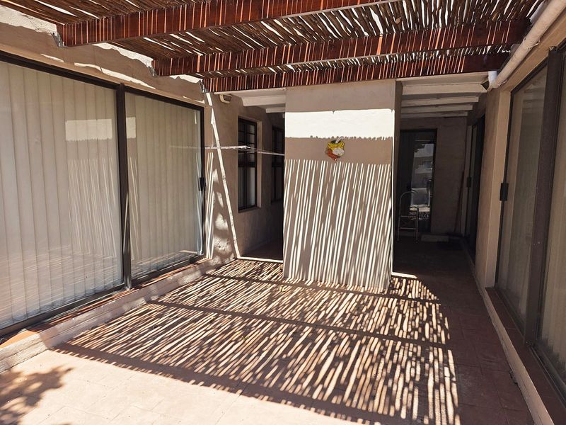 A covered patio area featuring a thatched pergola, tiled flooring, and multiple sliding glass door access points to the interior living spaces.