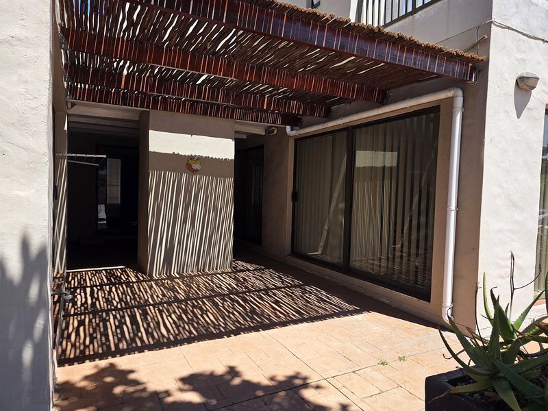 A covered patio area featuring a bamboo pergola, tiled flooring, and large sliding glass doors providing access to the interior.