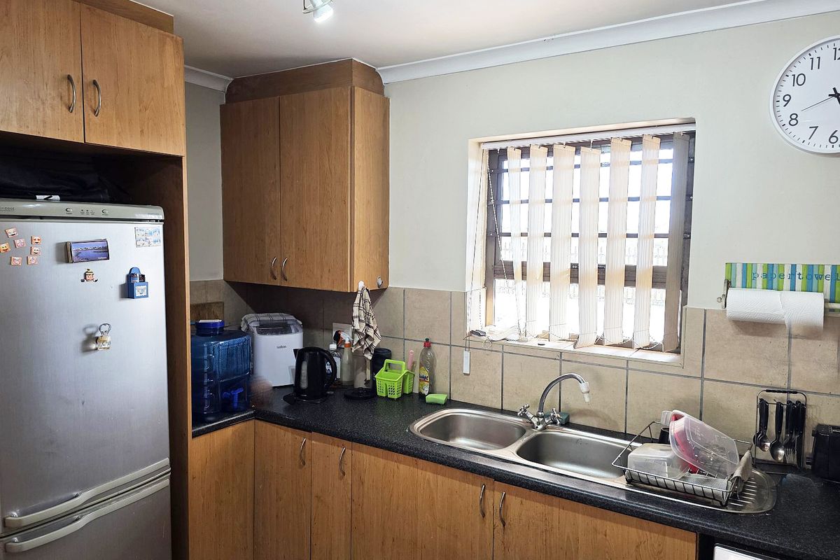 A functional kitchen featuring laminate cabinetry, a double bowl stainless steel sink, and tiled splashbacks, providing a practical workspace with natural light.