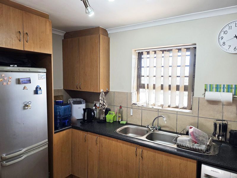 A functional kitchen featuring laminate cabinetry, a double bowl stainless steel sink, and tiled splashbacks, providing a practical workspace with natural light.