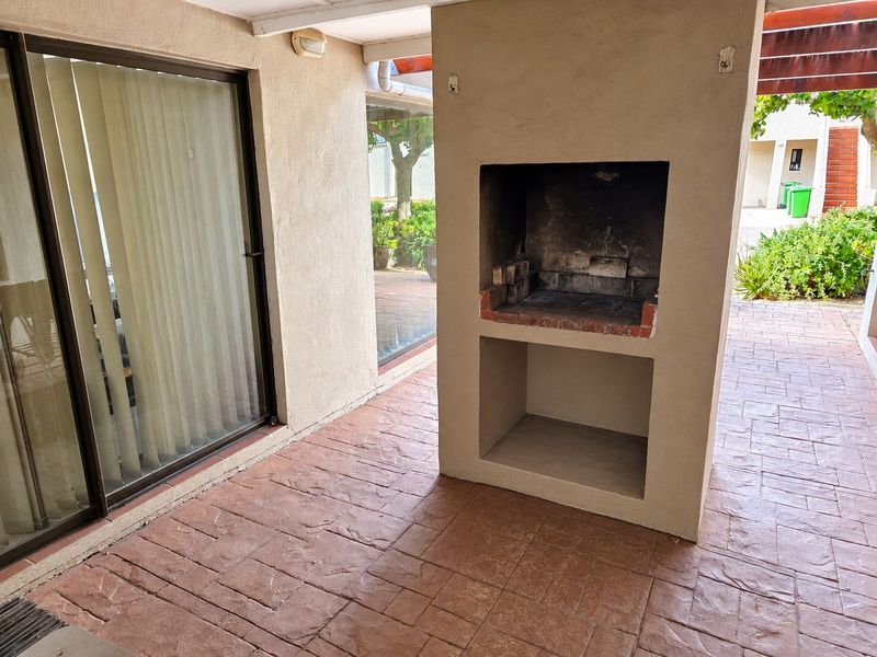 Covered patio area featuring a built-in brick braai and paved flooring, providing a functional outdoor entertainment space adjacent to the living area.