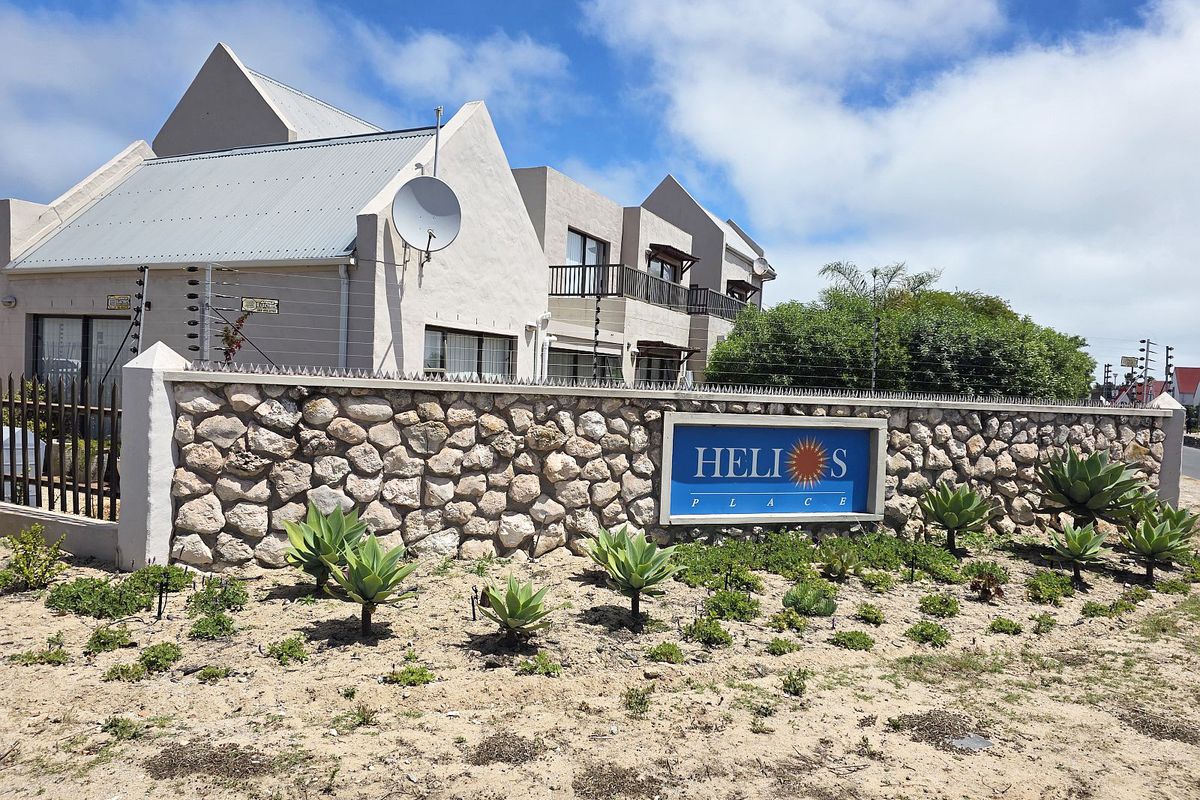 Exterior view of Helios Place apartment complex featuring a stone boundary wall, electric fencing, and modern architectural design with balconies.