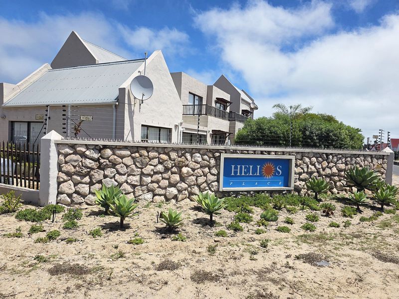 Exterior view of Helios Place apartment complex featuring a stone boundary wall, electric fencing, and modern architectural design with balconies.