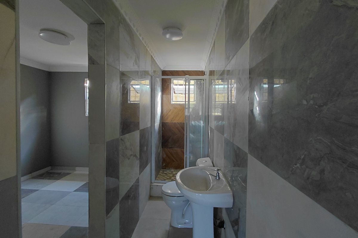A clean, tiled bathroom featuring a pedestal basin, toilet, and a separate shower enclosure with modern wall finishes.