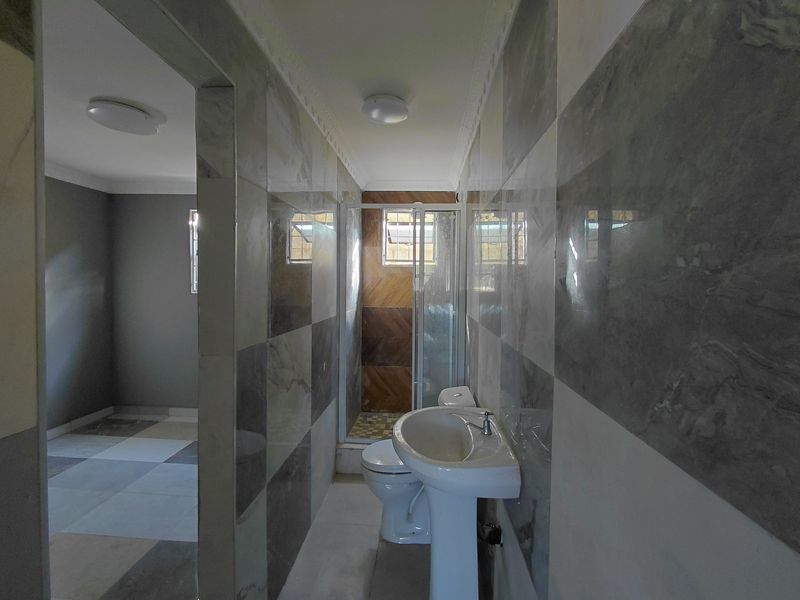 A clean, tiled bathroom featuring a pedestal basin, toilet, and a separate shower enclosure with modern wall finishes.