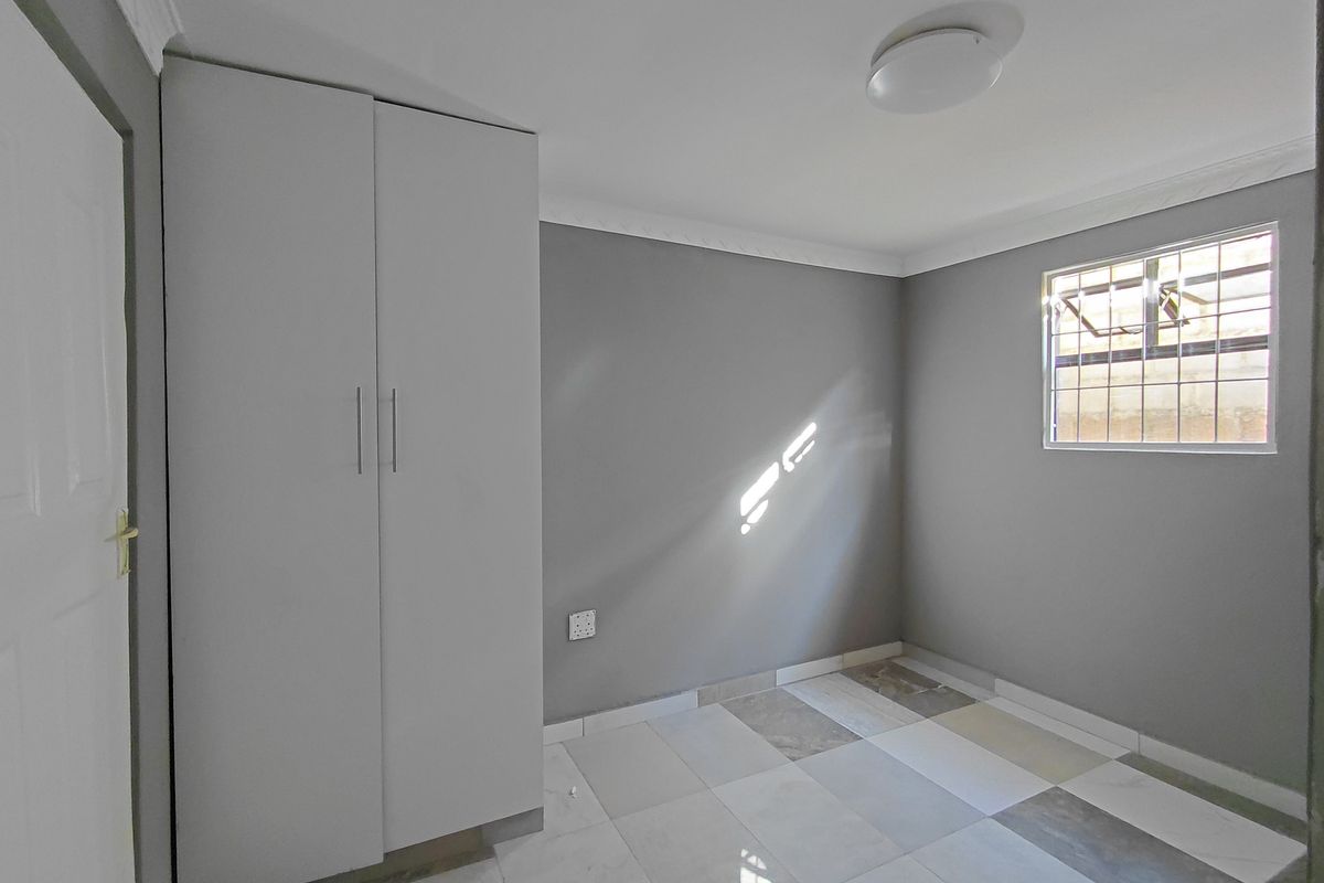 A clean, empty bedroom featuring neutral grey walls, modern tiled flooring, and a built-in wardrobe with security bars on the window.