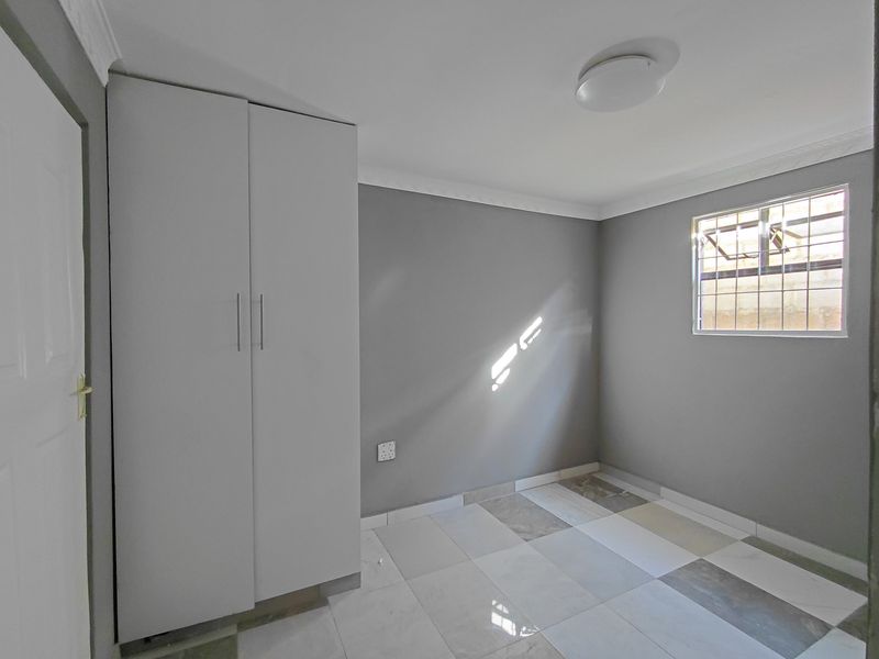 A clean, empty bedroom featuring neutral grey walls, modern tiled flooring, and a built-in wardrobe with security bars on the window.