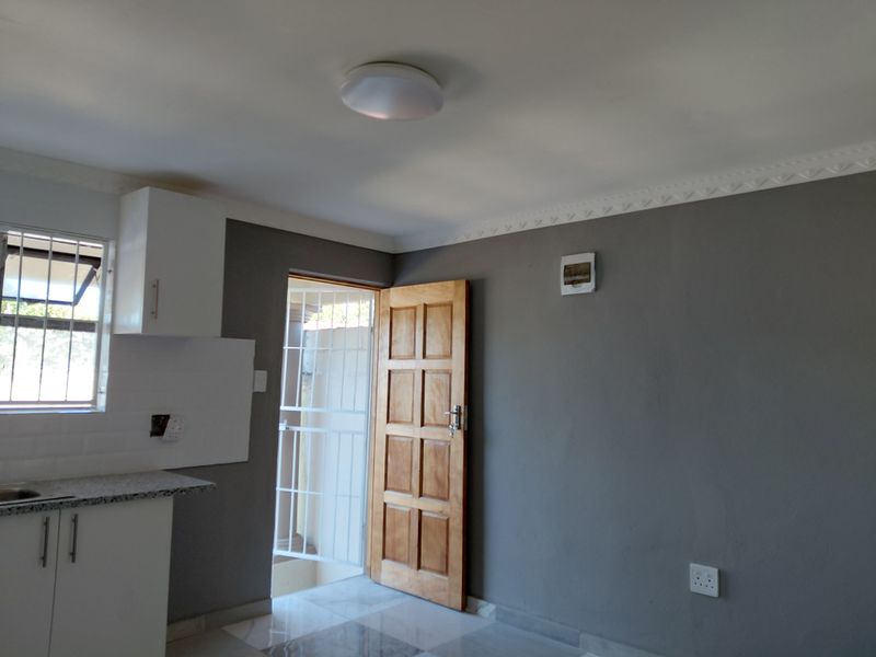 A clean, empty kitchen area featuring modern grey walls, white cabinetry, granite countertops, and direct access to an exterior security gate.