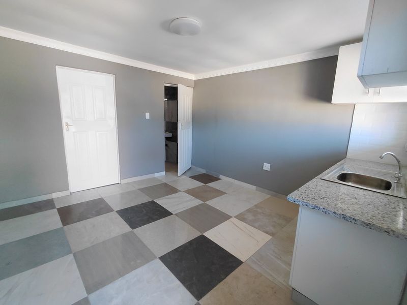 An open-plan kitchen area featuring granite countertops, a stainless steel sink, built-in cabinetry, and modern checkered tile flooring.