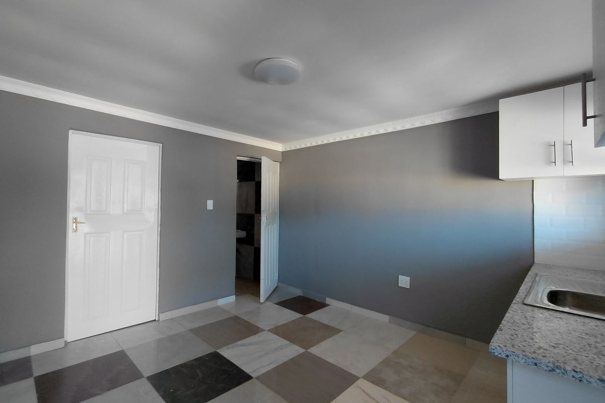 A clean, empty kitchen area featuring modern grey walls, patterned tiled flooring, built-in cabinetry with granite countertops, and a stainless steel sink.