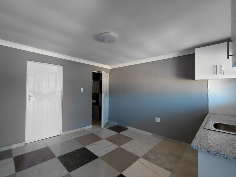 A clean, empty kitchen area featuring modern grey walls, patterned tiled flooring, built-in cabinetry with granite countertops, and a stainless steel sink.