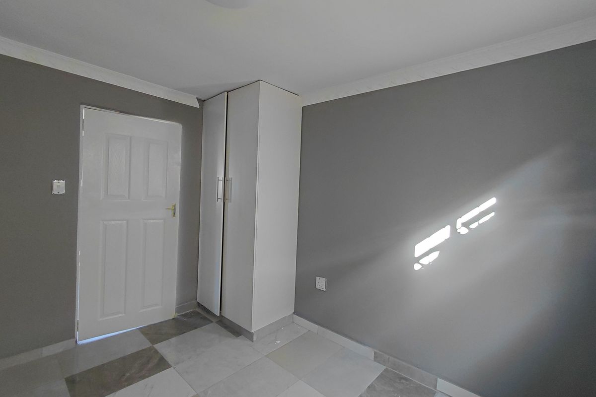 A clean, empty bedroom featuring neutral grey walls, tiled flooring, and a built-in white wardrobe.