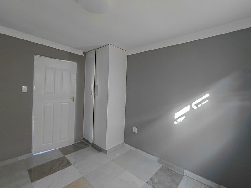 A clean, empty bedroom featuring neutral grey walls, tiled flooring, and a built-in white wardrobe.