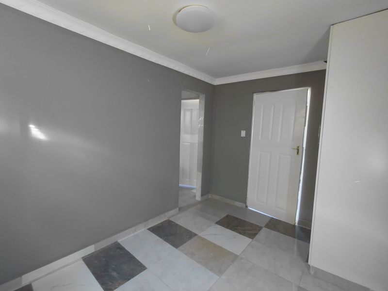 An empty bedroom featuring grey painted walls, tiled flooring, built-in cupboards, and ceiling cornice detailing.
