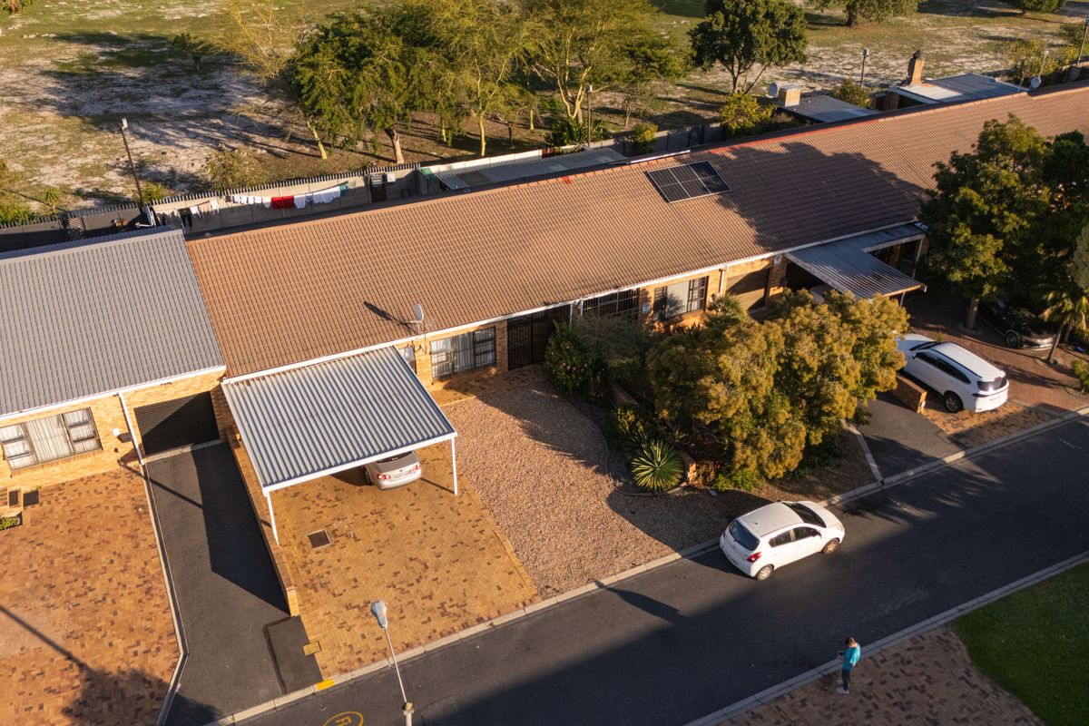 Aerial view of a residential property featuring a tiled roof with solar panels, a paved driveway, and a covered carport.