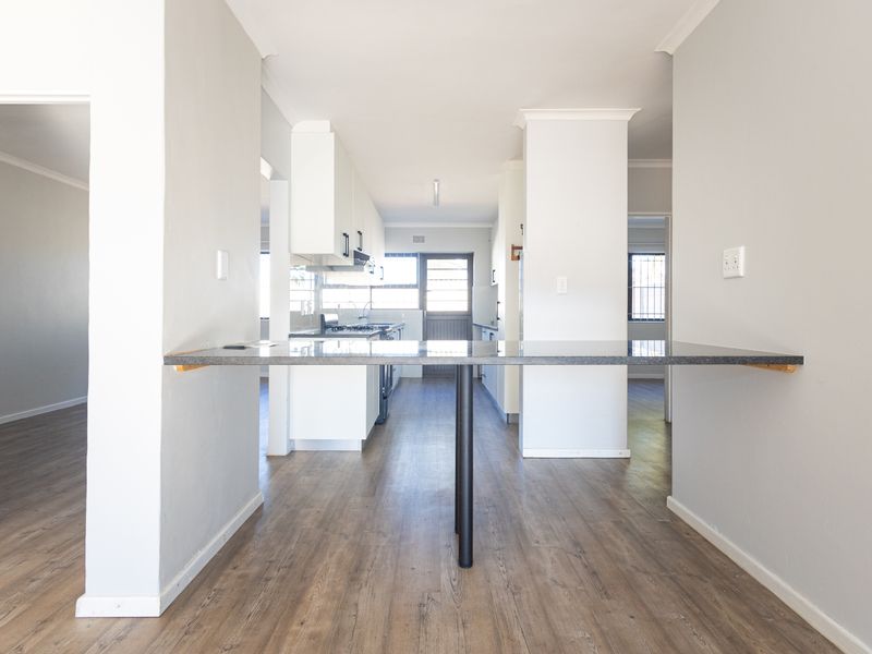 A bright, open-plan kitchen featuring modern laminate flooring, white cabinetry, and a functional breakfast bar, leading to a rear exterior door.