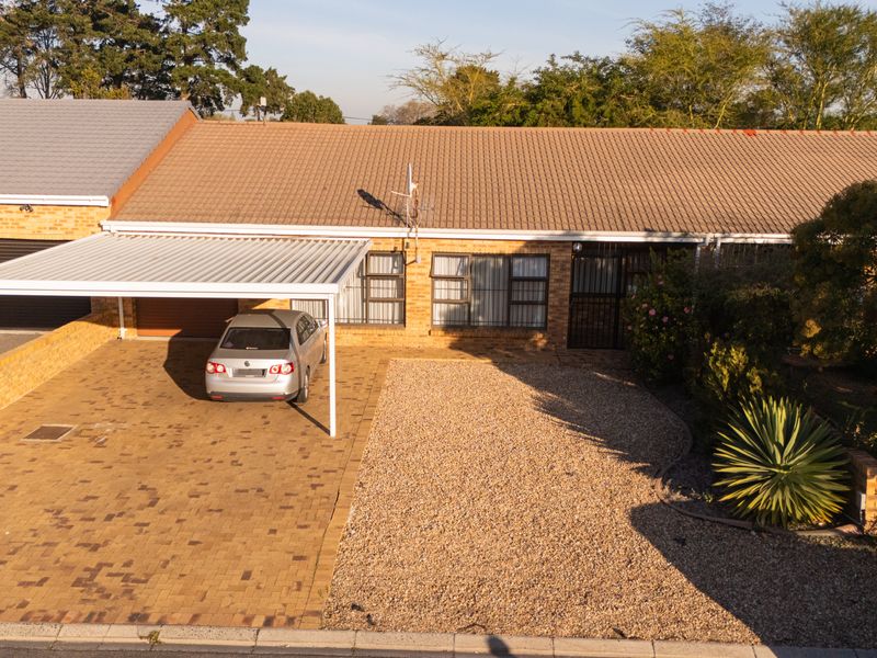Front elevation of a brick house featuring a tiled roof, paved driveway with a carport, and a low-maintenance gravel garden area.