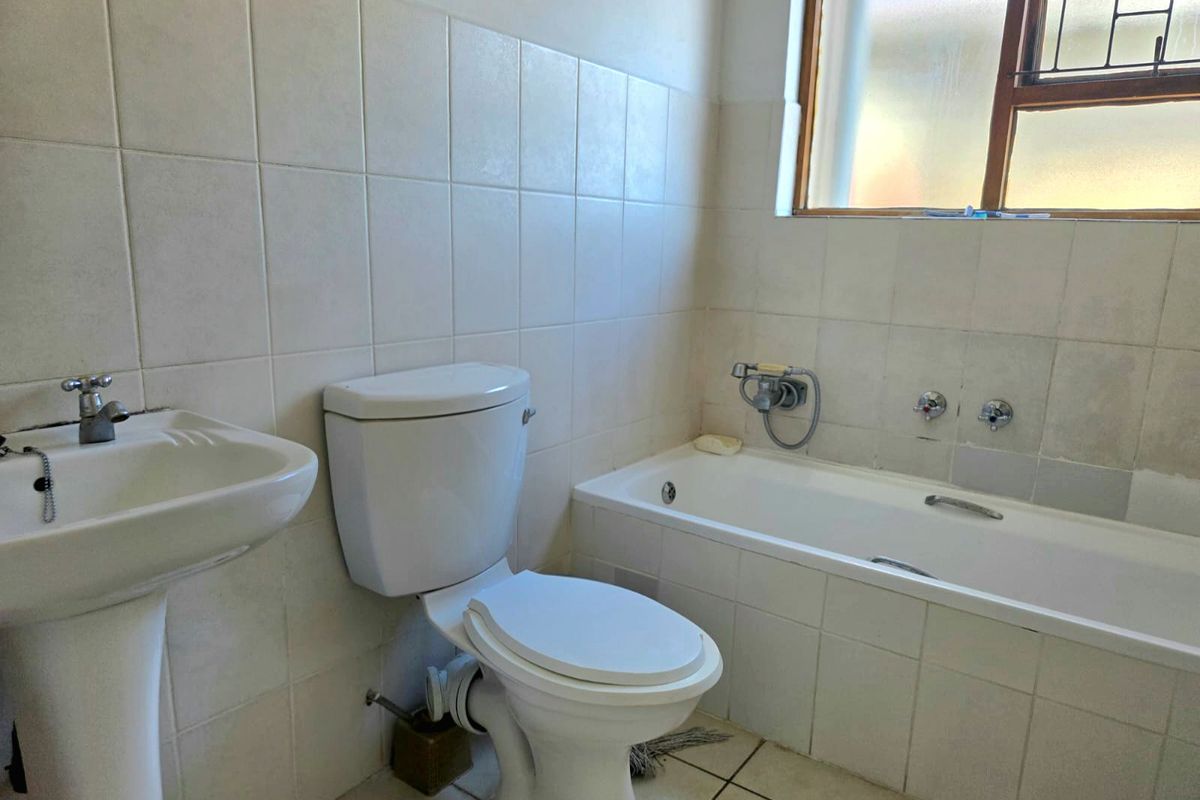 A functional bathroom featuring a pedestal basin, toilet, and bathtub with tiled walls and flooring, offering a blank canvas for modern renovation.