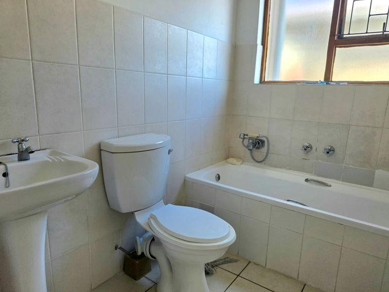 A functional bathroom featuring a pedestal basin, toilet, and bathtub with tiled walls and flooring, offering a blank canvas for modern renovation.