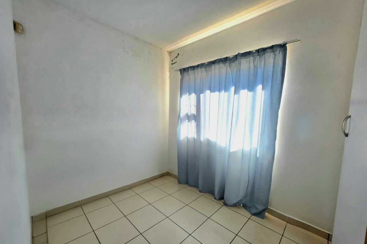 An empty bedroom featuring tiled flooring and a window with a curtain rod, showing signs of wear on the wall surfaces.