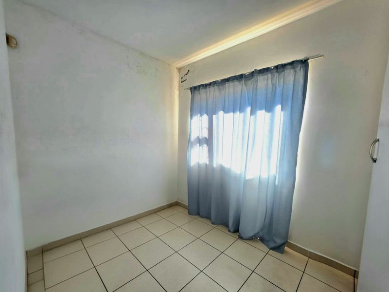 An empty bedroom featuring tiled flooring and a window with a curtain rod, showing signs of wear on the wall surfaces.