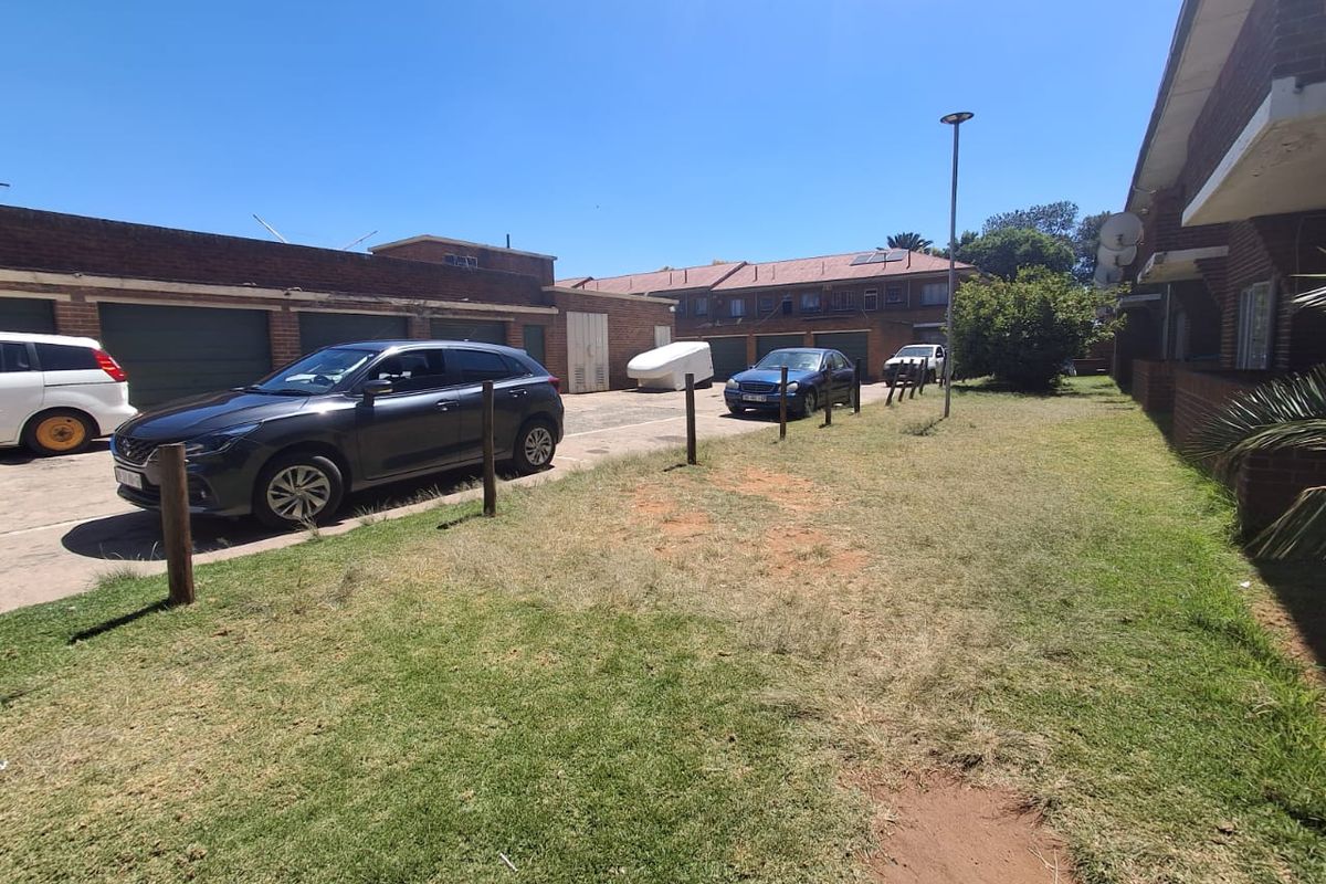 Rear exterior view of the townhouse complex featuring a shared driveway, brick garage units, and an open lawn area.