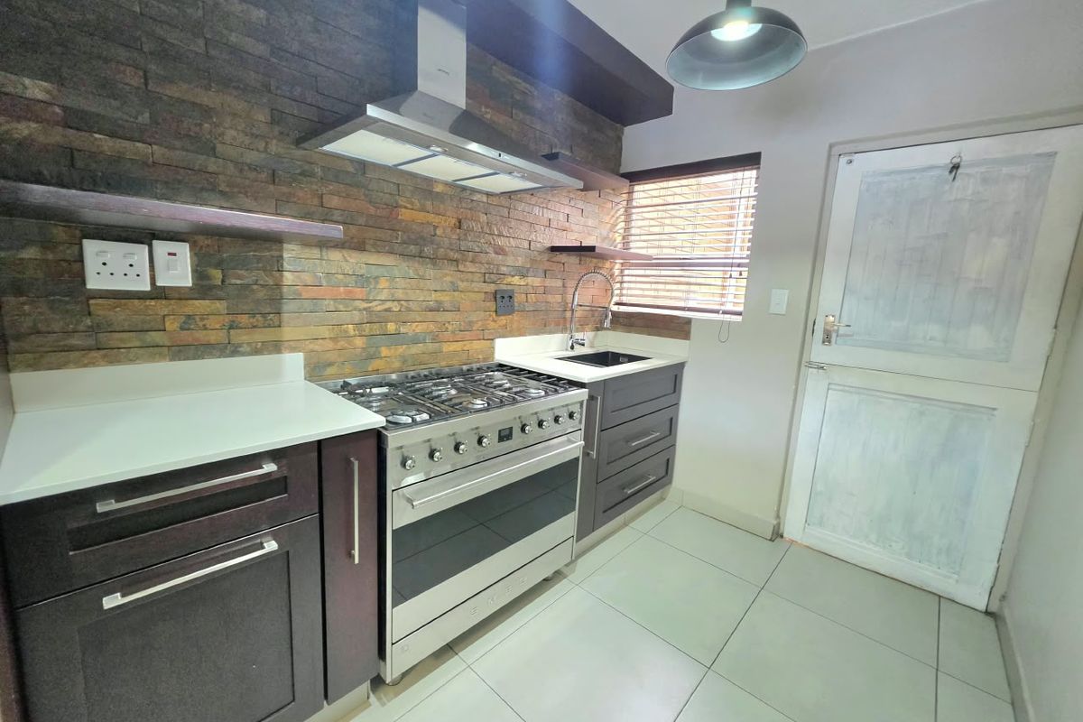Modern kitchen featuring a striking stone veneer backsplash, stainless steel gas stove with extractor, quartz countertops, and sleek dark cabinetry.