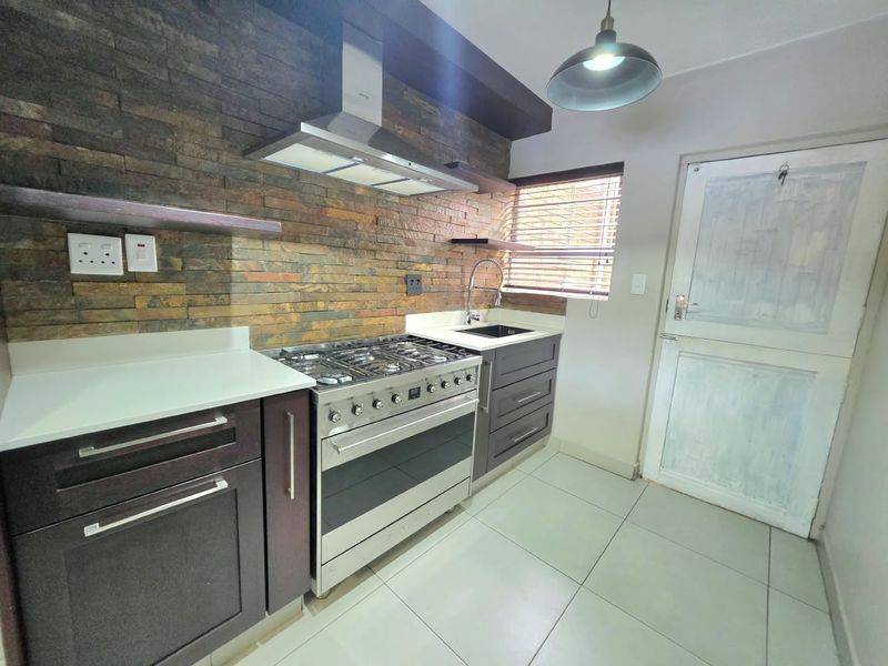 Modern kitchen featuring a striking stone veneer backsplash, stainless steel gas stove with extractor, quartz countertops, and sleek dark cabinetry.