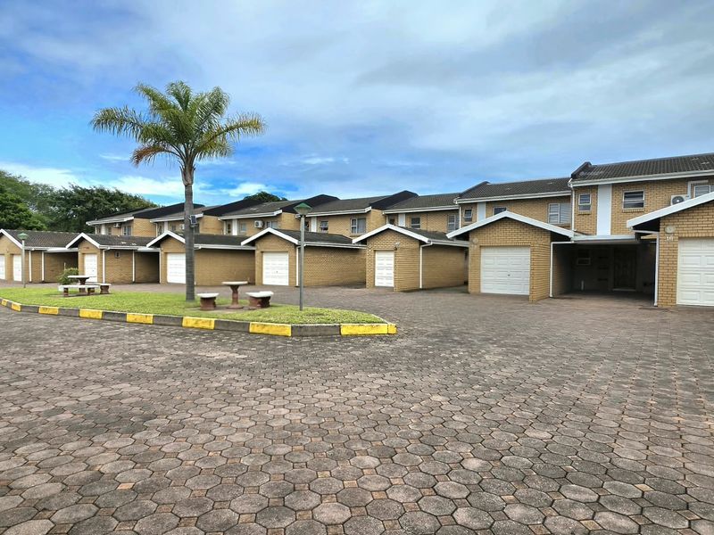 Exterior view of a townhouse complex featuring brick facades, tiled roofs, and individual garage units with a paved driveway.