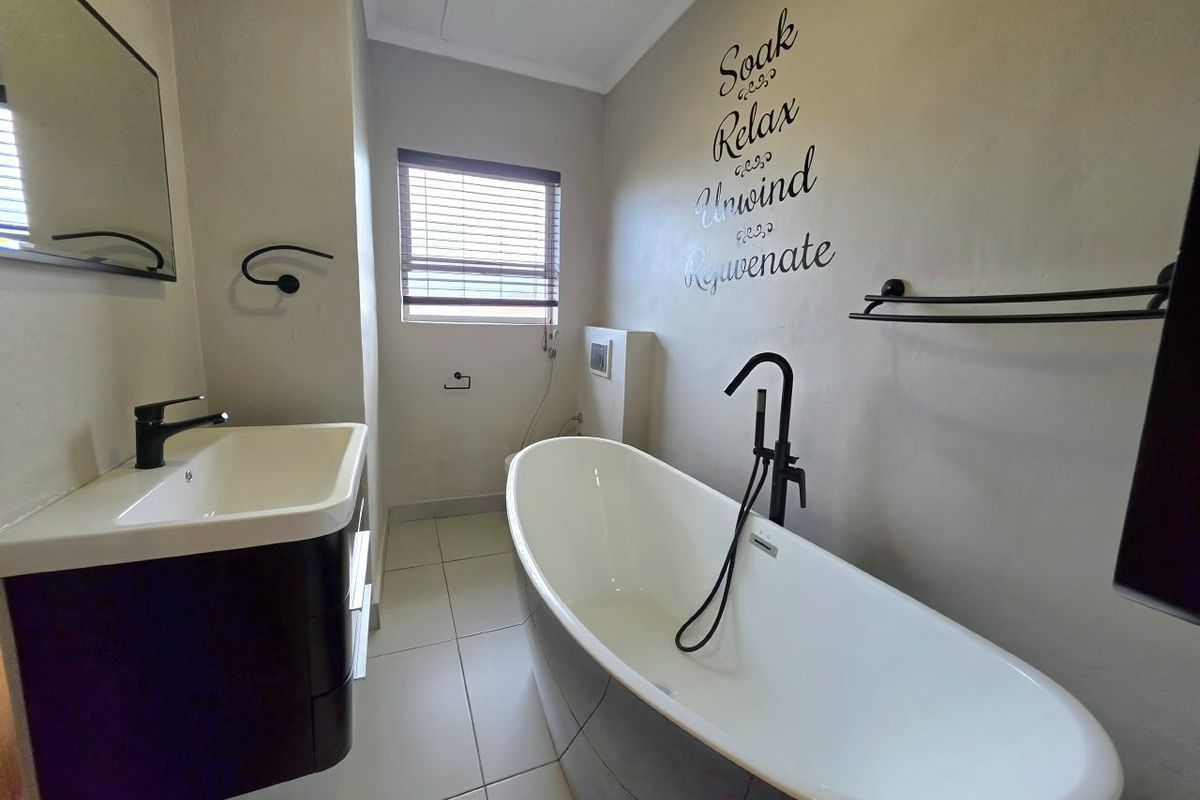 Modern bathroom featuring a sleek freestanding bathtub with black matte fixtures, a wall-mounted vanity basin, and neutral tiled flooring.