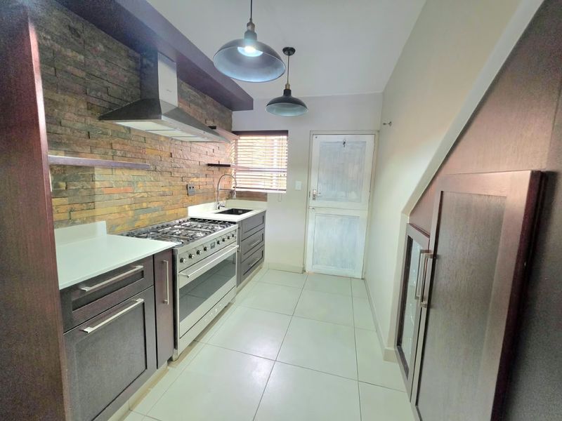 Modern kitchen featuring a striking stone veneer backsplash, stainless steel gas stove, extractor fan, and ample built-in cabinetry with tiled flooring.