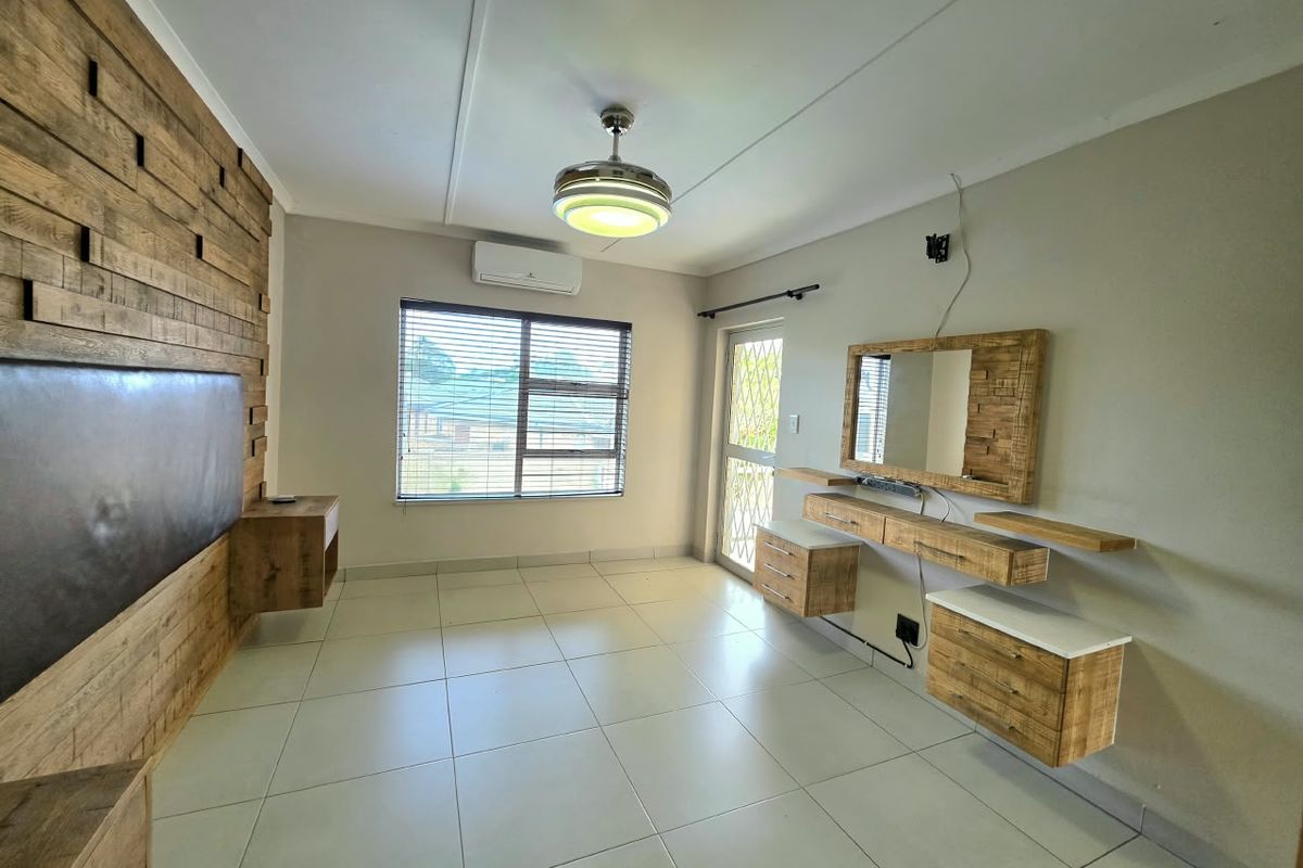 A spacious bedroom featuring a built-in wooden vanity, a decorative timber headboard wall, tiled flooring, and an integrated air conditioning unit.
