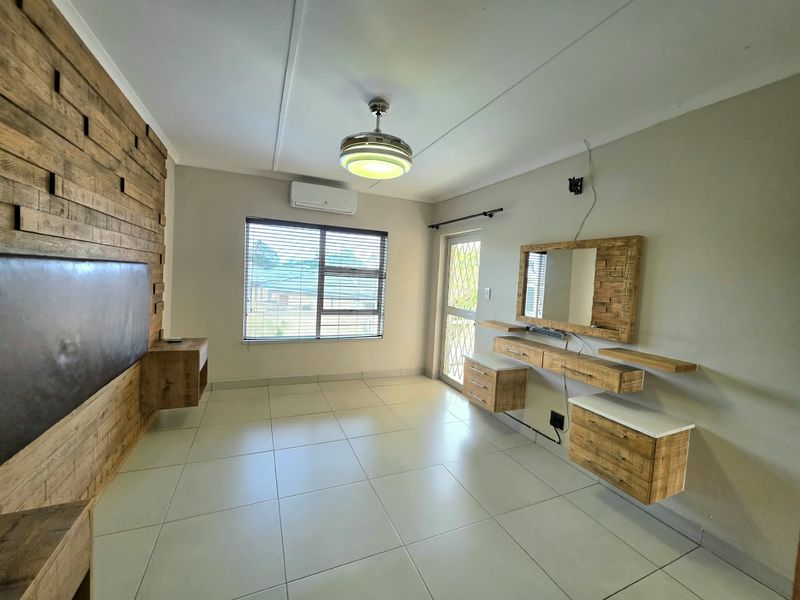 A spacious bedroom featuring a built-in wooden vanity, a decorative timber headboard wall, tiled flooring, and an integrated air conditioning unit.