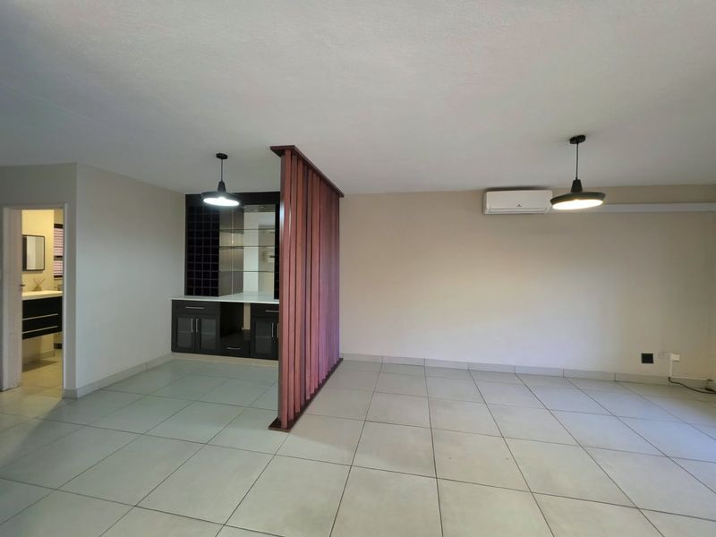 Spacious living area featuring tiled flooring, a built-in bar unit, decorative timber slat divider, and a wall-mounted air conditioning unit.