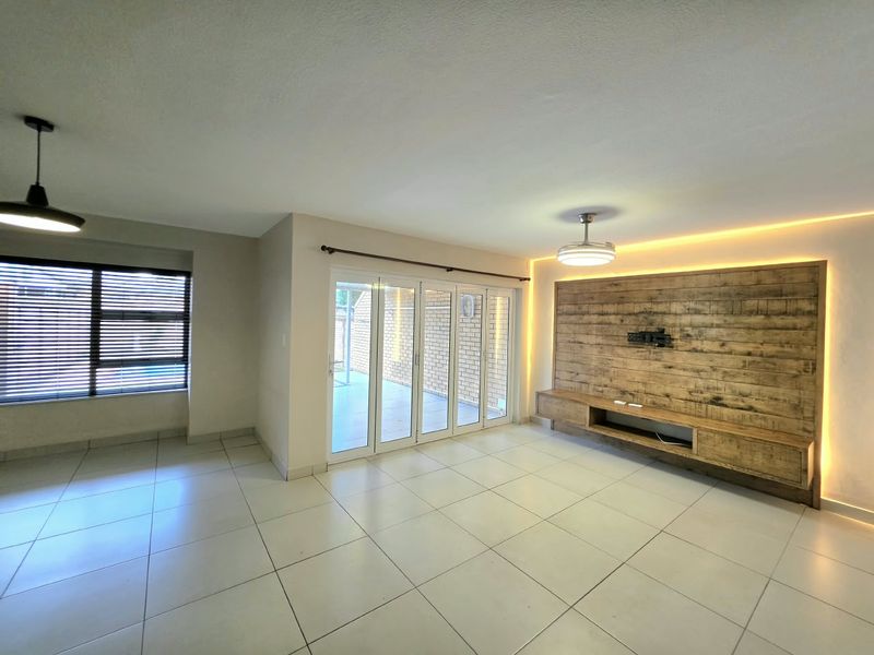 Spacious living room featuring tiled floors, built-in wooden media cabinetry with ambient LED lighting, and large aluminium sliding doors leading to the patio.