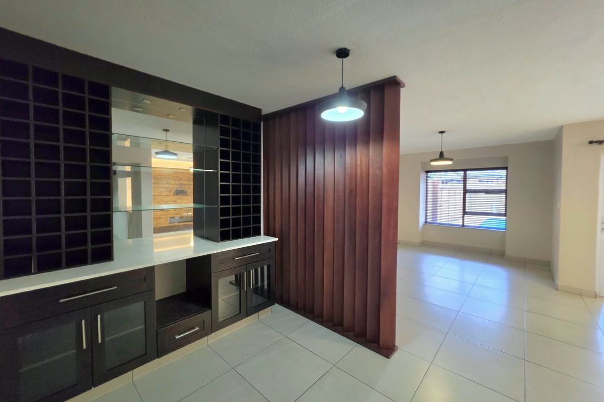 Spacious living area featuring a custom built-in bar with wine storage, a decorative timber slat room divider, and neutral tiled flooring throughout.