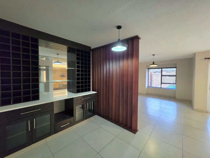 Spacious living area featuring a custom built-in bar with wine storage, a decorative timber slat room divider, and neutral tiled flooring throughout.