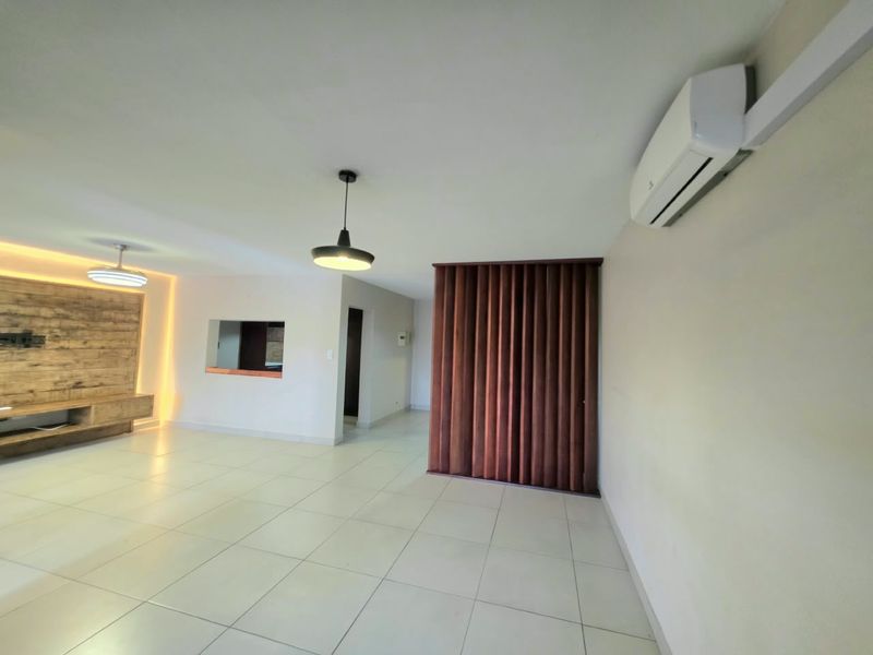 Spacious living area featuring tiled floors, a split-system air conditioner, custom timber slat room divider, and a built-in media console with ambient feature lighting.