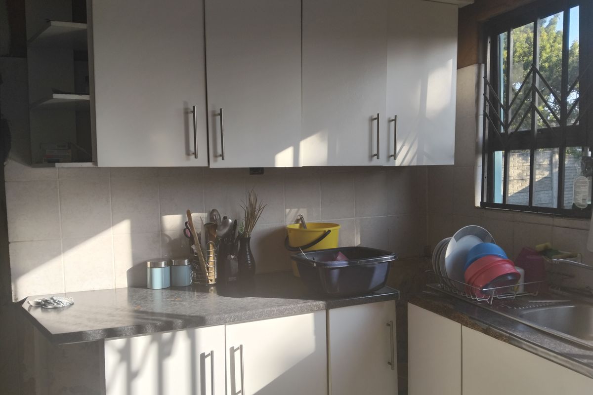 A functional kitchen featuring white cabinetry, laminate countertops, a tiled backsplash, and a stainless steel sink with natural light from the window.