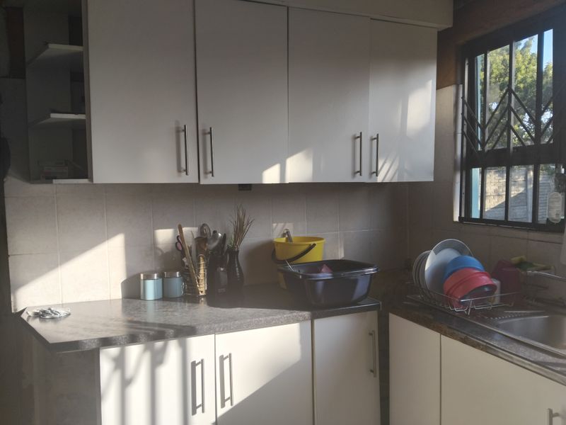 A functional kitchen featuring white cabinetry, laminate countertops, a tiled backsplash, and a stainless steel sink with natural light from the window.